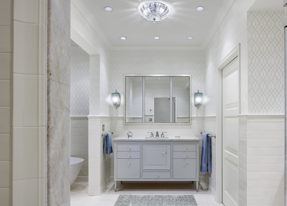 Imagen de cuarto de baño clásico renovado con puertas de armario grises, baldosas y/o azulejos blancos, paredes grises, lavabo bajoencimera, suelo blanco, encimeras blancas y armarios con paneles con relieve
