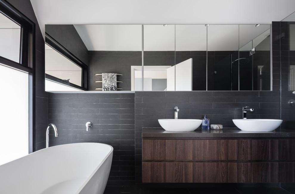 Design ideas for a contemporary ensuite bathroom in Sydney with flat-panel cabinets, dark wood cabinets, a freestanding bath, an alcove shower, black tiles, black walls, a vessel sink, a hinged door and black worktops.