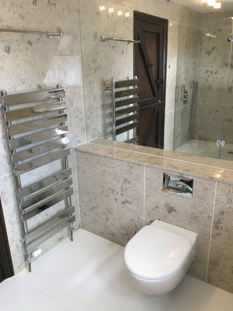 Design ideas for a medium sized contemporary shower room bathroom in London with flat-panel cabinets, white cabinets, a walk-in shower, a wall mounted toilet, beige tiles, limestone tiles, beige walls, a submerged sink, limestone worktops, white floors and a hinged door.