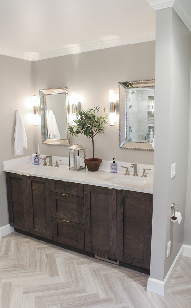 Example of a large transitional master limestone tile limestone floor and beige floor bathroom design in Austin with brown cabinets, quartz countertops, a hinged shower door, shaker cabinets, gray walls and an undermount sink