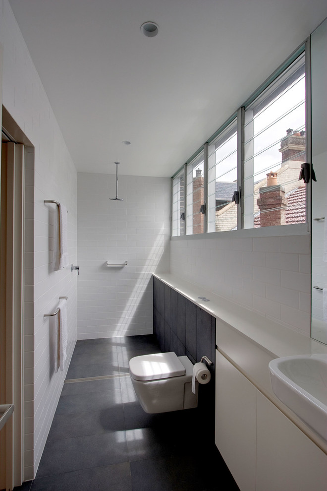 Inredning av ett modernt litet badrum, med släta luckor, vita skåp, en öppen dusch, en vägghängd toalettstol, vit kakel, tunnelbanekakel, med dusch som är öppen, klinkergolv i keramik och svart golv