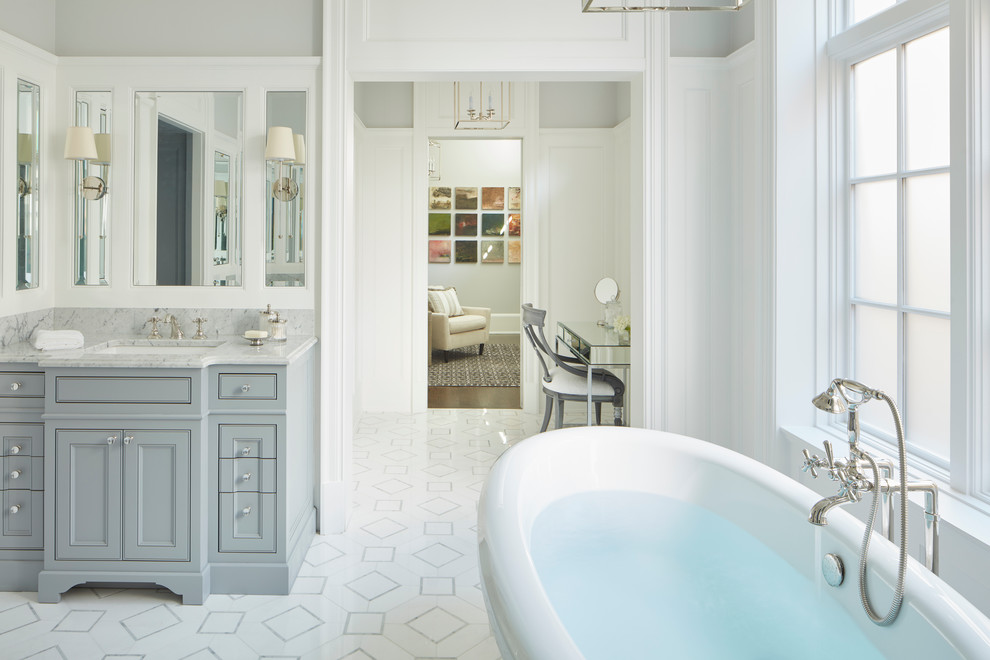 Diseño de cuarto de baño clásico con armarios con rebordes decorativos, puertas de armario grises, bañera exenta, paredes grises y lavabo bajoencimera