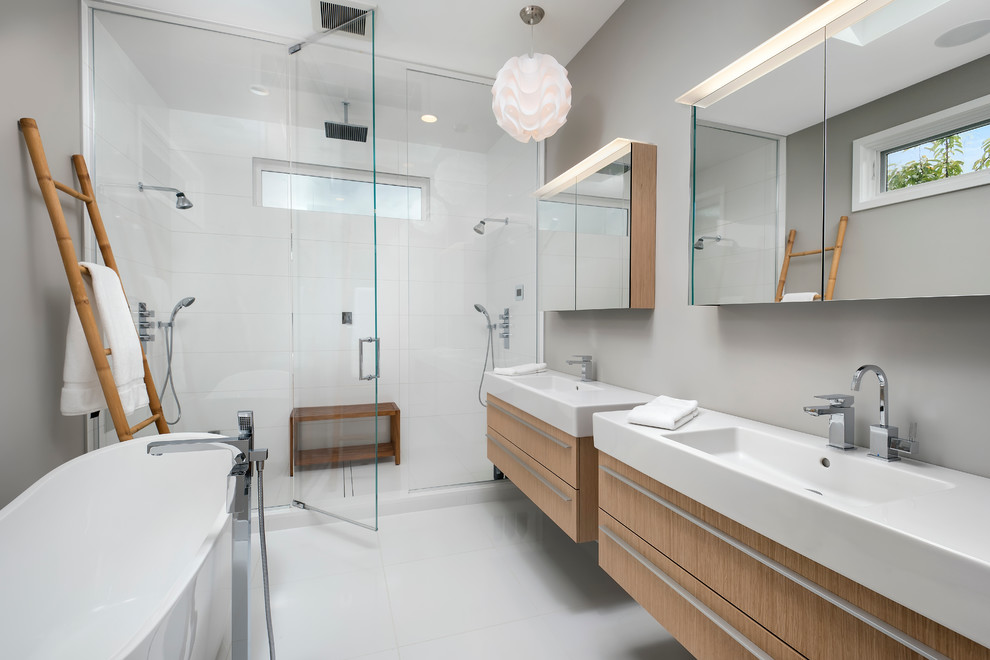 Inredning av ett modernt en-suite badrum, med släta luckor, skåp i ljust trä, ett fristående badkar, en dusch i en alkov, grå väggar, ett integrerad handfat, vit kakel, porslinskakel, klinkergolv i porslin och dusch med gångjärnsdörr