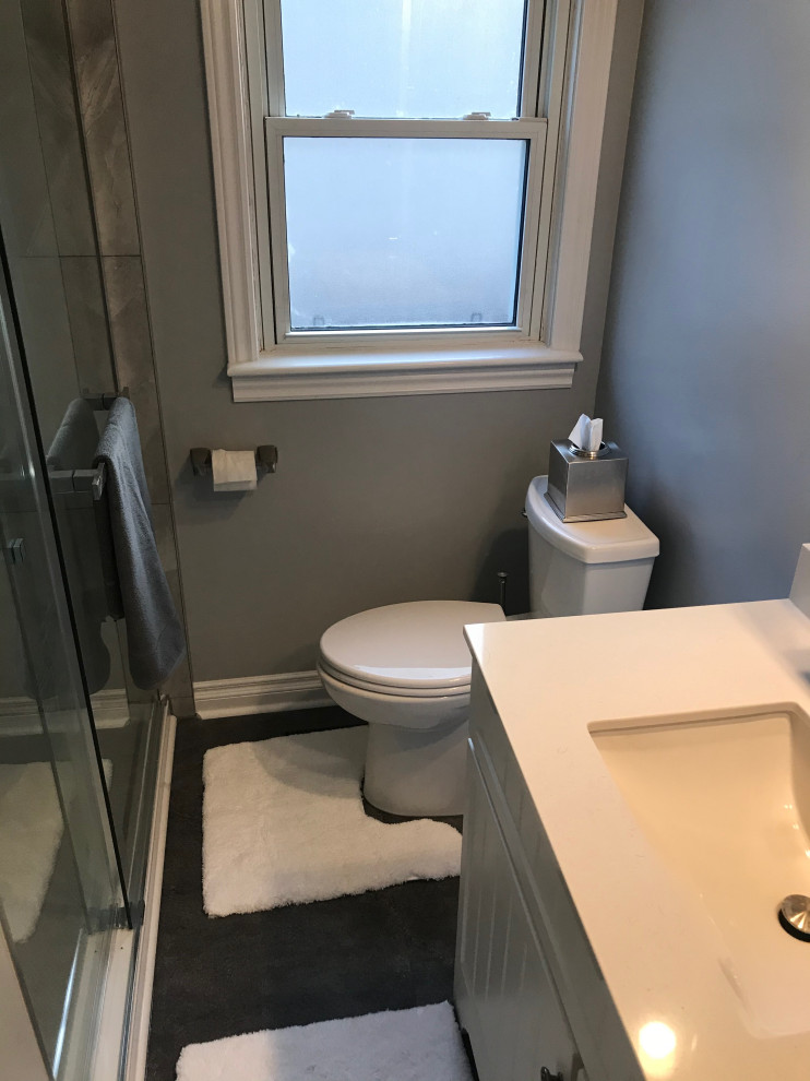 Inredning av ett litet vit vitt badrum, med vita skåp, en dusch i en alkov, en toalettstol med separat cisternkåpa, grå kakel, porslinskakel, grå väggar, vinylgolv, grått golv och dusch med skjutdörr