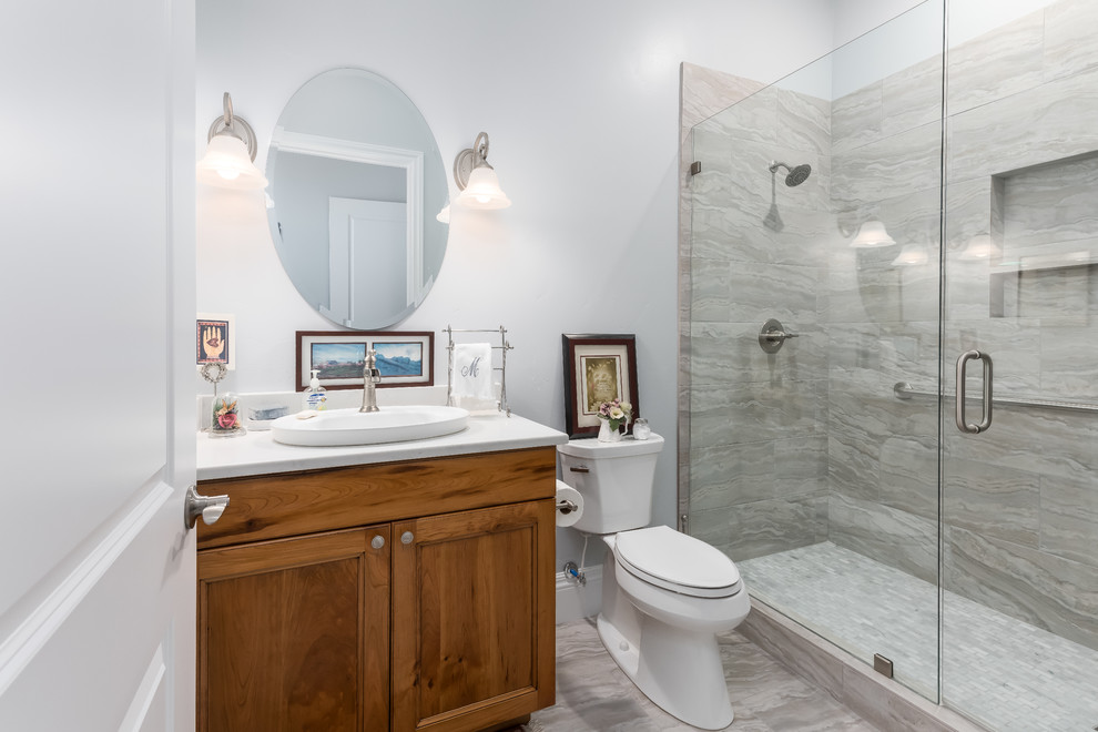 Bild på ett litet vintage vit vitt badrum med dusch, med en toalettstol med separat cisternkåpa, grå kakel, grå väggar, bänkskiva i kvarts, luckor med infälld panel, skåp i mellenmörkt trä, ett nedsänkt handfat och grått golv