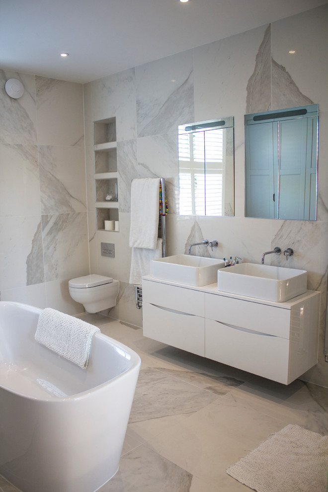 На фото: главная ванная комната среднего размера в современном стиле с отдельно стоящей ванной, инсталляцией, настольной раковиной, плоскими фасадами и белыми фасадами