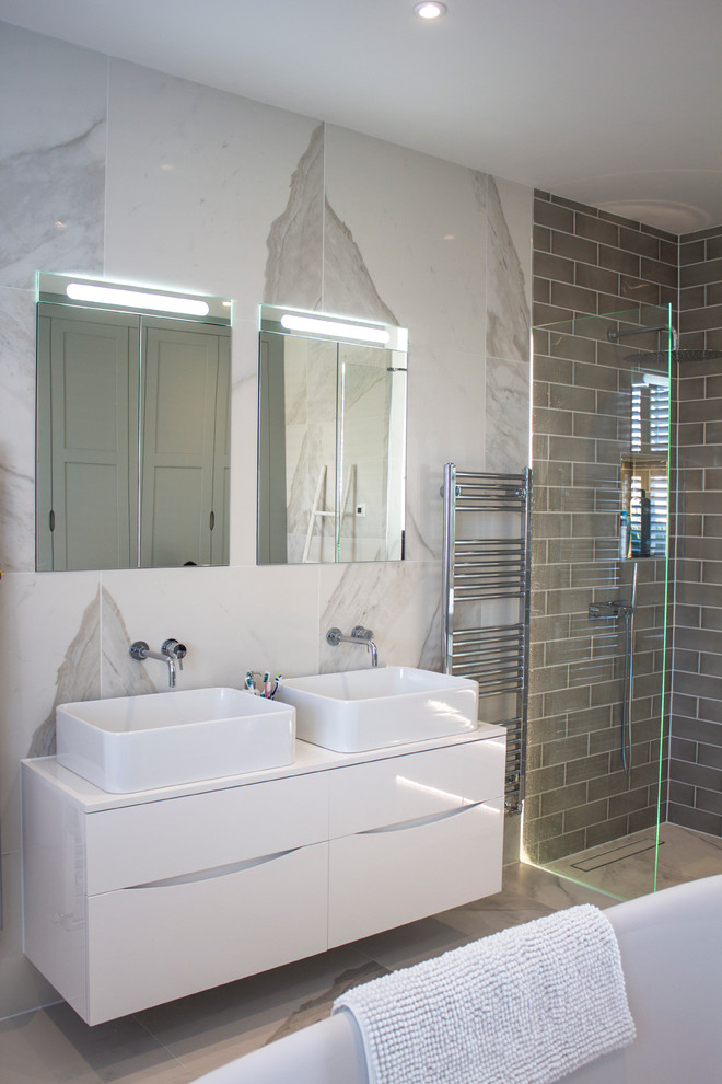 Foto de cuarto de baño principal actual de tamaño medio con bañera exenta, ducha abierta, sanitario de pared, baldosas y/o azulejos de porcelana y baldosas y/o azulejos grises