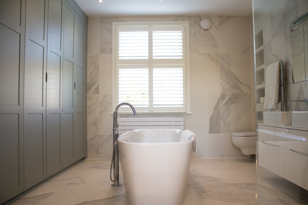 Imagen de cuarto de baño principal actual de tamaño medio con bañera exenta, ducha abierta, sanitario de pared, baldosas y/o azulejos de porcelana y baldosas y/o azulejos blancos