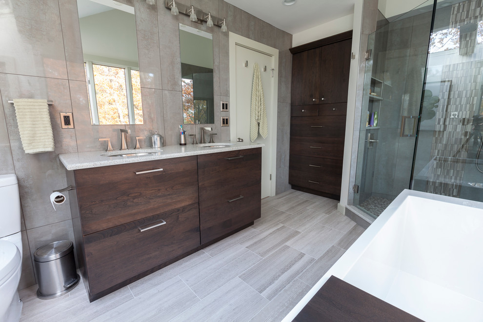 Exemple d'une grande salle de bain principale moderne en bois foncé avec un lavabo encastré, un placard à porte plane, un plan de toilette en verre recyclé, une baignoire indépendante, une douche d'angle, WC séparés, un carrelage gris, des carreaux de porcelaine, un mur gris et un sol en travertin.