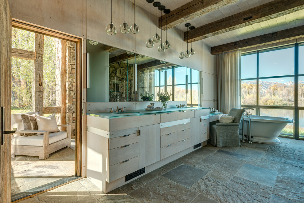 Rustik inredning av ett stort en-suite badrum, med ett fristående badkar, flerfärgad kakel, stenkakel, ett nedsänkt handfat, bänkskiva i glas, släta luckor, beige skåp, beige väggar och klinkergolv i keramik