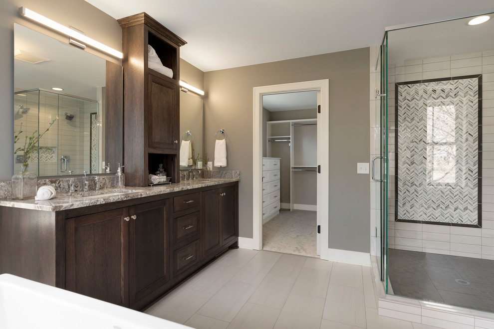 Photo of a large classic ensuite bathroom in Minneapolis with shaker cabinets, dark wood cabinets, a freestanding bath, a corner shower, a two-piece toilet, grey walls, ceramic flooring, a submerged sink, granite worktops, grey floors, a hinged door and multi-coloured worktops.