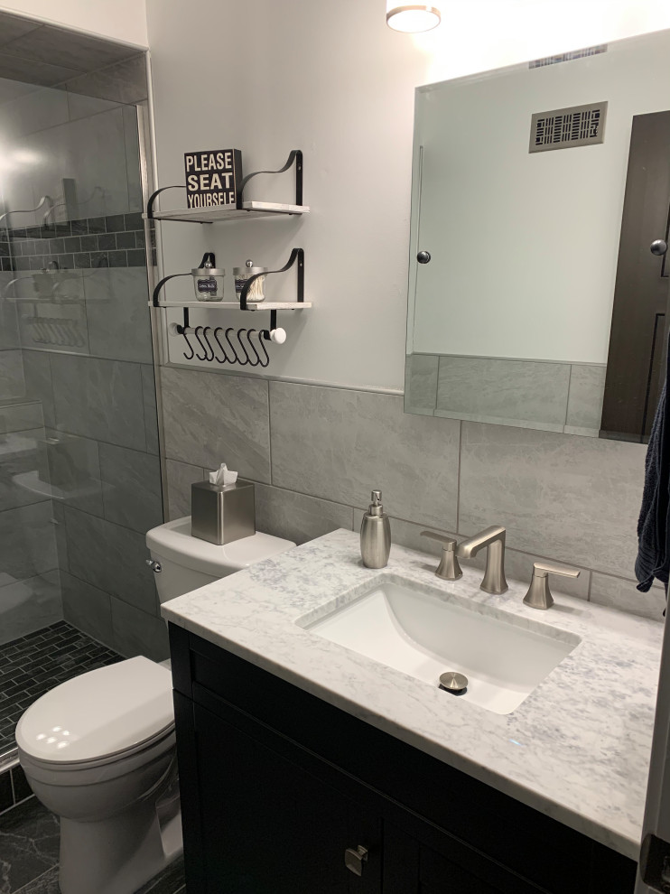 Photo of a medium sized contemporary shower room bathroom in Minneapolis with dark wood cabinets, an alcove shower, a one-piece toilet, grey tiles, porcelain tiles, grey walls, porcelain flooring, a submerged sink, marble worktops, black floors, a hinged door, grey worktops, a single sink, a freestanding vanity unit and wainscoting.