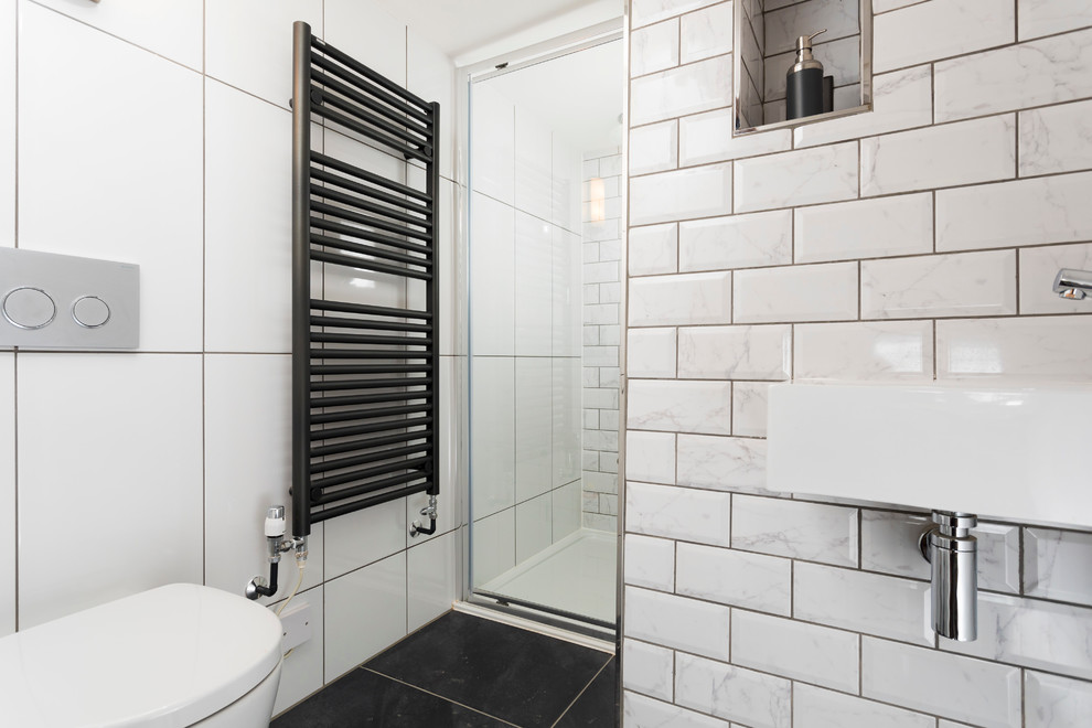 Foto på ett litet rustikt en-suite badrum, med släta luckor, vita skåp, en kantlös dusch, en vägghängd toalettstol, vit kakel, porslinskakel, vita väggar, klinkergolv i porslin, ett väggmonterat handfat och bänkskiva i akrylsten