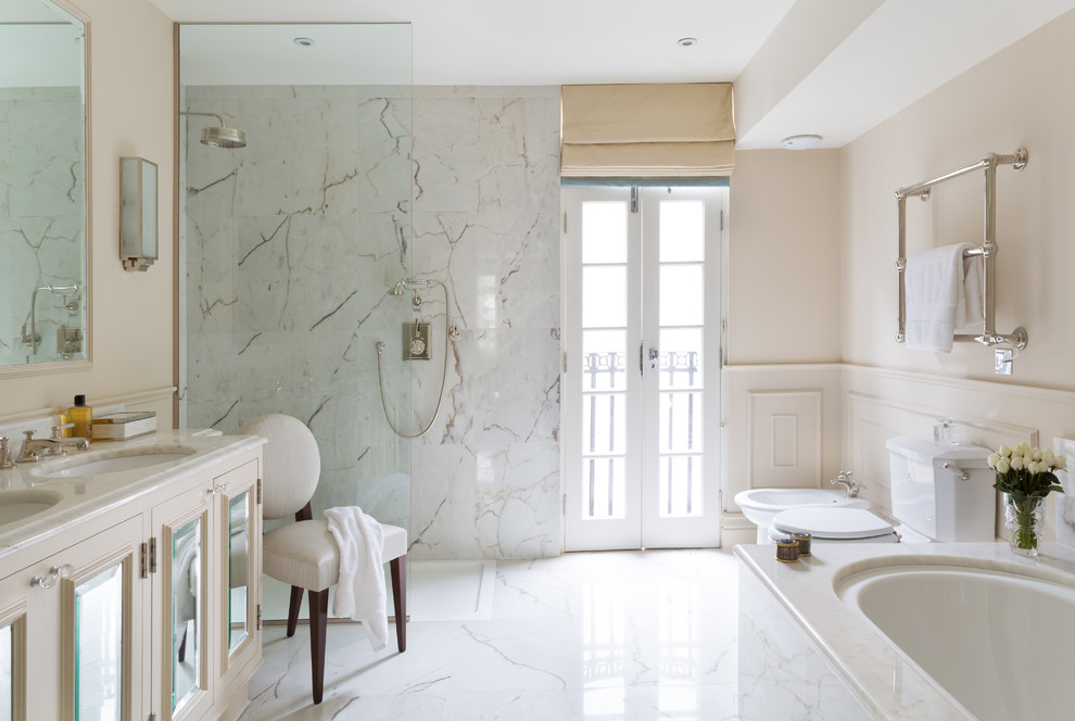 Photo of a large classic ensuite bathroom in London with white cabinets, a walk-in shower, white tiles, stone tiles, white walls, marble flooring, an open shower, shaker cabinets, a built-in bath, a two-piece toilet, an integrated sink, marble worktops and beige worktops.