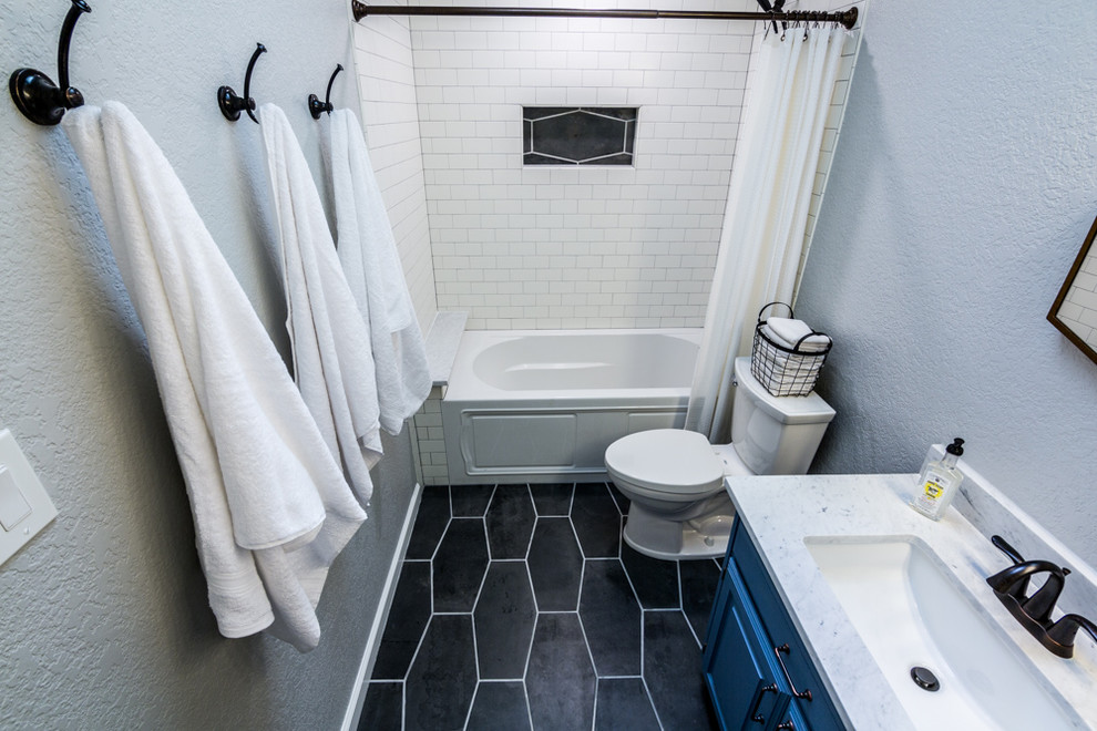 Cette image montre une salle de bain bohème de taille moyenne avec un placard avec porte à panneau surélevé, des portes de placard bleues, une baignoire en alcôve, un combiné douche/baignoire, un carrelage blanc, un carrelage métro, un mur gris, un sol en carrelage de porcelaine, un lavabo encastré, un plan de toilette en marbre, un sol gris et une cabine de douche avec un rideau.