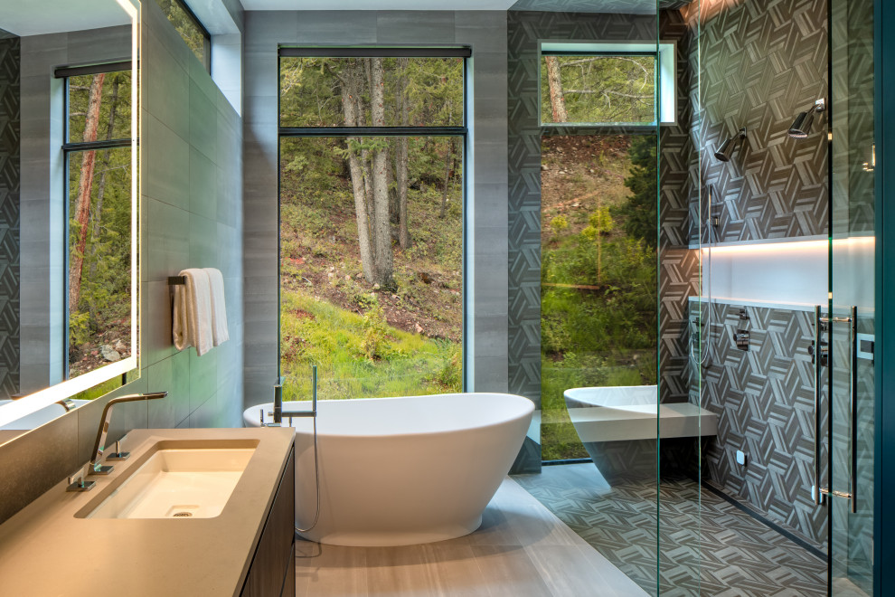 Idée de décoration pour une salle de bain design en bois foncé avec un placard à porte plane, une baignoire indépendante, une douche à l'italienne, un carrelage gris, un lavabo encastré, un sol gris, une cabine de douche à porte battante et un plan de toilette gris.