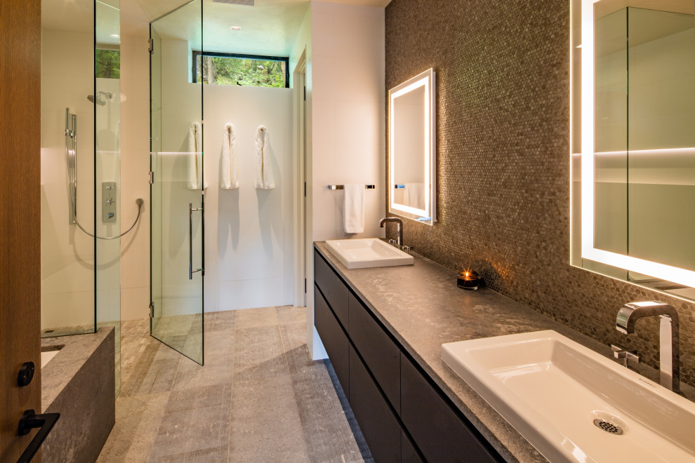 Modelo de cuarto de baño doble contemporáneo con armarios con paneles lisos, bañera encastrada sin remate, ducha esquinera, baldosas y/o azulejos grises, baldosas y/o azulejos en mosaico, lavabo encastrado, suelo gris y encimeras grises