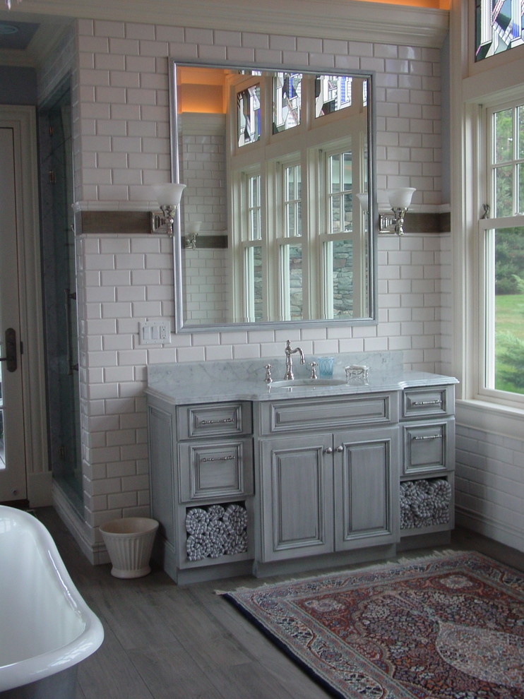 Medium sized classic ensuite bathroom in Boston with raised-panel cabinets, grey cabinets, a freestanding bath, a two-piece toilet, white tiles, metro tiles, white walls, medium hardwood flooring, a submerged sink, marble worktops and grey floors.