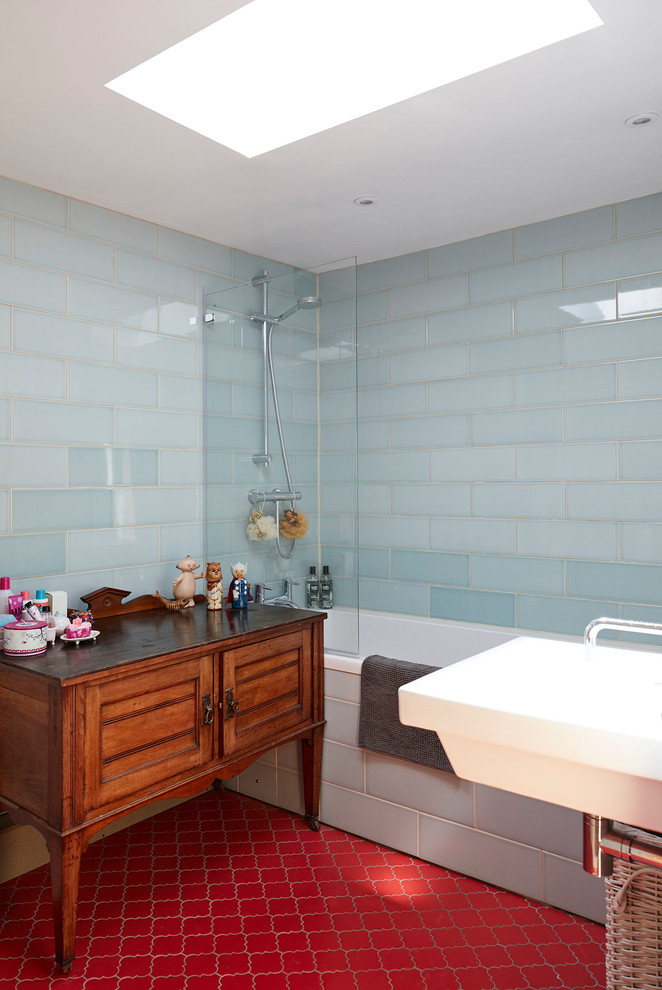 Photo of a medium sized rural ensuite bathroom in Hertfordshire with blue tiles, ceramic flooring, a wall-mounted sink, red floors, medium wood cabinets, an alcove bath, a shower/bath combination, metro tiles, an open shower and recessed-panel cabinets.