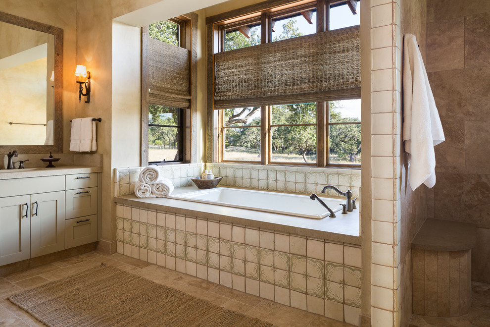 Cette image montre une salle de bain chalet avec un placard à porte shaker, des portes de placard beiges, une baignoire posée et un carrelage beige.