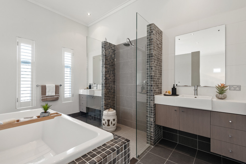 Idée de décoration pour une salle de bain design avec un placard à porte plane, des portes de placard grises, une baignoire posée, un carrelage gris, un mur blanc, un sol noir et un plan de toilette blanc.