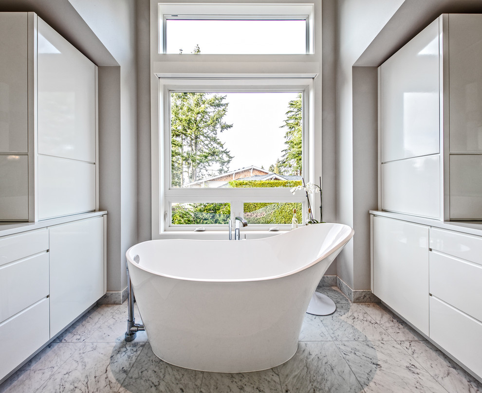 Exemple d'une grande salle de bain principale tendance avec un placard à porte plane, des portes de placard blanches, une baignoire indépendante, un carrelage blanc, un carrelage de pierre, un mur blanc, un sol en marbre, un lavabo encastré et un plan de toilette en quartz modifié.