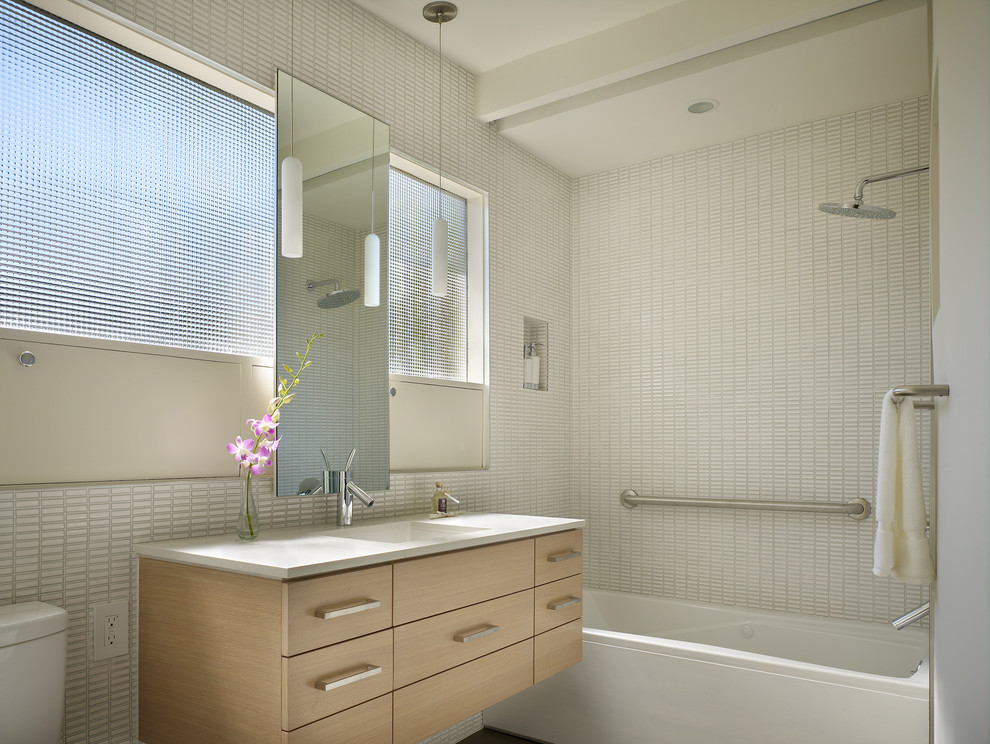 Immagine di una stanza da bagno design con lavabo sottopiano, ante lisce, ante in legno chiaro, vasca ad alcova, vasca/doccia, piastrelle bianche e piastrelle a mosaico