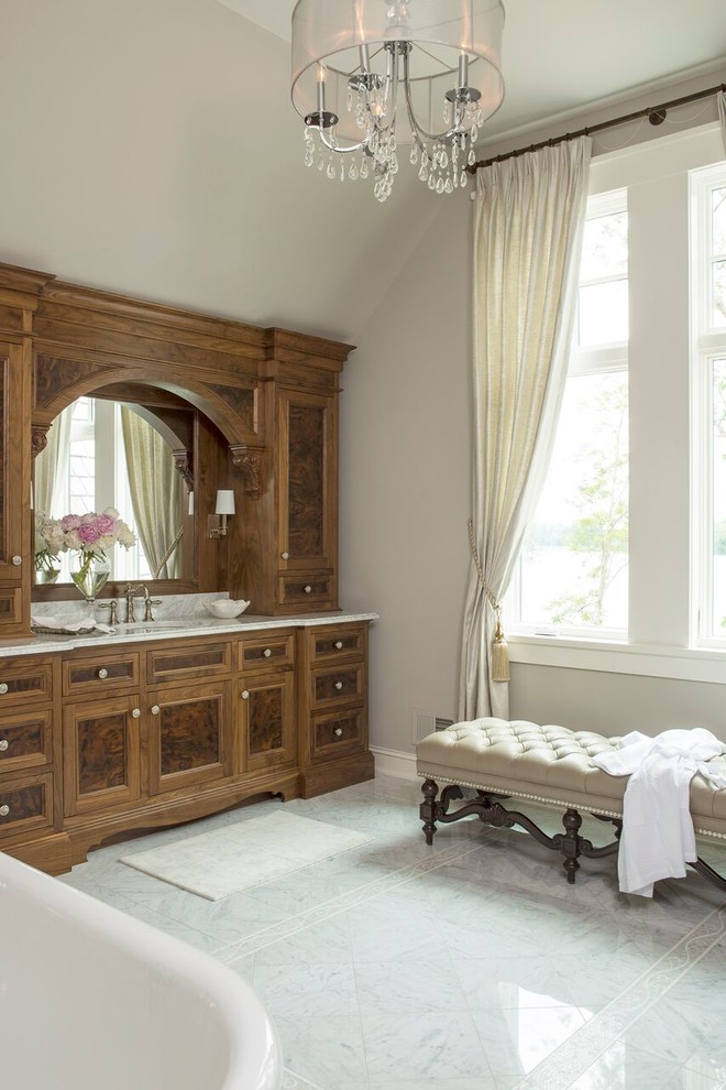 Inredning av ett klassiskt badrum, med ett undermonterad handfat, luckor med infälld panel, skåp i mörkt trä, marmorbänkskiva, en dusch i en alkov, en toalettstol med separat cisternkåpa, vit kakel och stenkakel