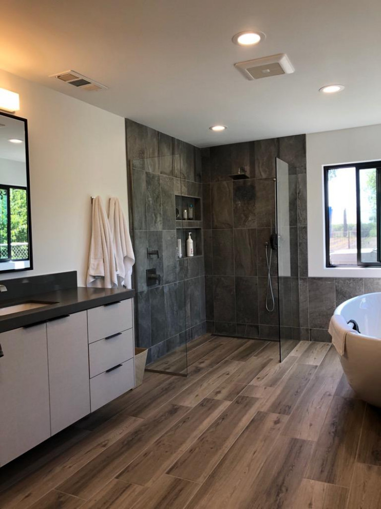 Photo of a large contemporary ensuite bathroom in Sacramento with flat-panel cabinets, beige cabinets, a freestanding bath, a built-in shower, a bidet, grey tiles, ceramic tiles, white walls, ceramic flooring, a built-in sink, quartz worktops, grey floors, an open shower, black worktops, a single sink and a floating vanity unit.
