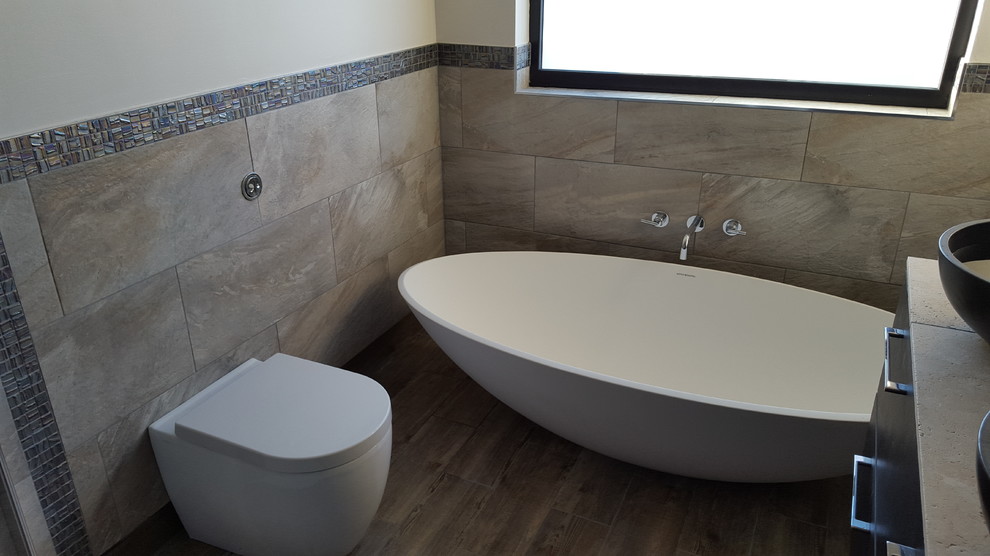 Design ideas for a medium sized contemporary ensuite bathroom in Other with dark wood cabinets, a freestanding bath, beige tiles, stone tiles, beige walls, porcelain flooring, a vessel sink and limestone worktops.