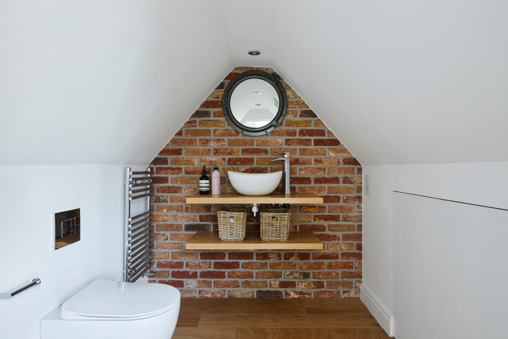 Photo of a medium sized classic bathroom in London with white walls, a vaulted ceiling, medium hardwood flooring, a vessel sink, wooden worktops, brown floors, beige worktops, a single sink and brick walls.