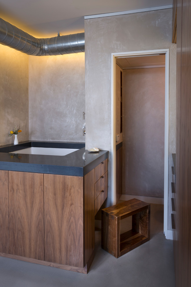 Cette image montre une petite salle de bain principale minimaliste en bois foncé avec un lavabo intégré, un placard à porte plane, un plan de toilette en béton, une baignoire encastrée, une douche ouverte, WC suspendus, un mur beige et sol en béton ciré.