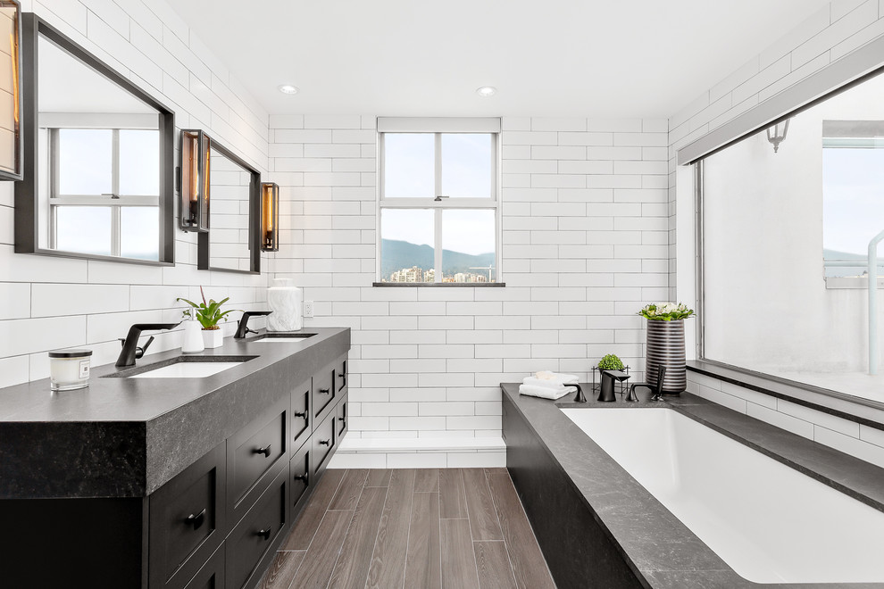 Design ideas for a medium sized contemporary ensuite bathroom in Vancouver with black cabinets, a submerged bath, white tiles, metro tiles, a submerged sink, engineered stone worktops, brown floors, black worktops and shaker cabinets.