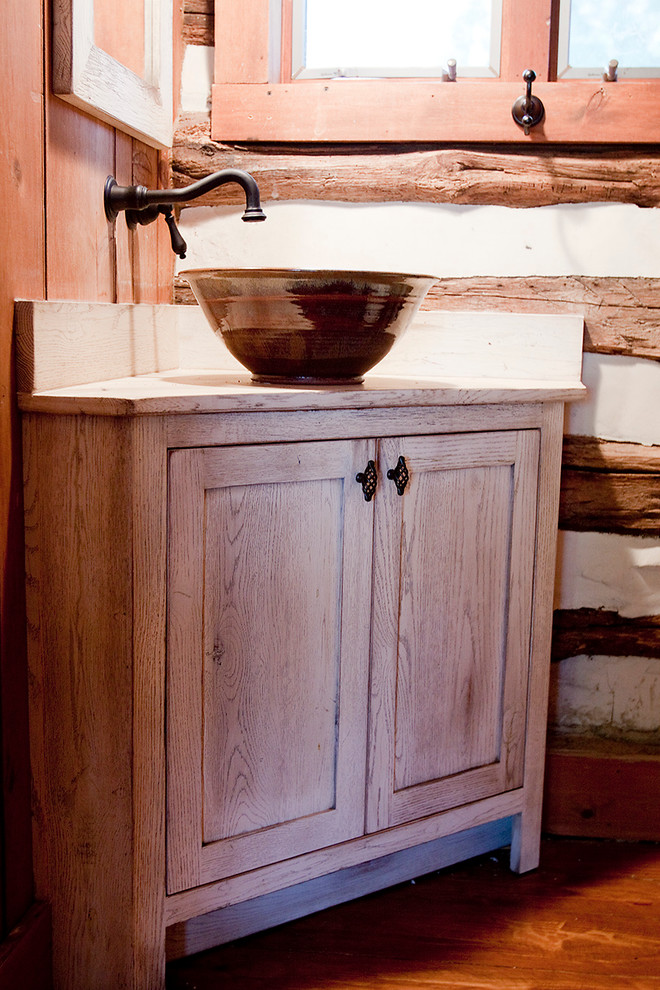 Modelo de cuarto de baño campestre pequeño con lavabo sobreencimera, armarios con paneles lisos, puertas de armario con efecto envejecido y encimera de madera