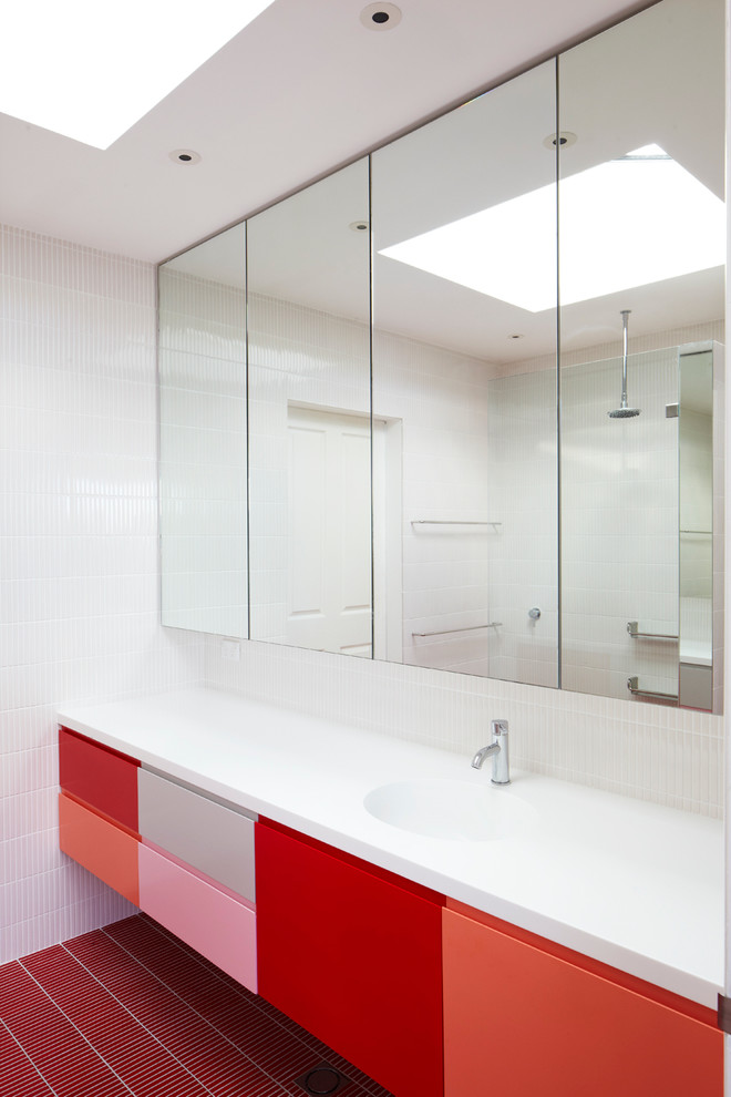 Modern inredning av ett mellanstort en-suite badrum, med ett integrerad handfat, släta luckor, röda skåp, bänkskiva i akrylsten, vit kakel, mosaikgolv och rött golv