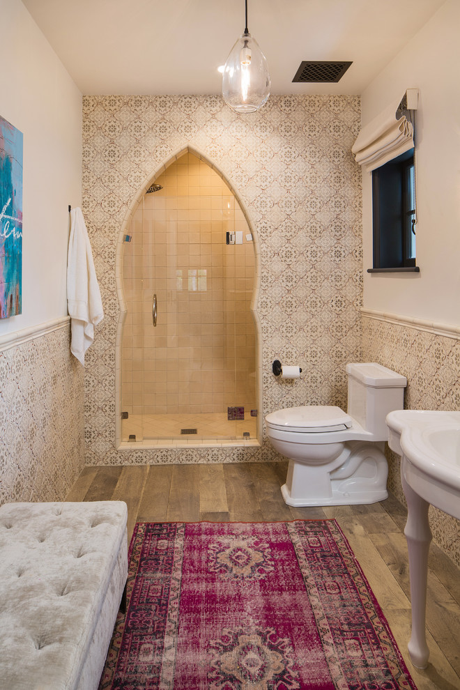 Mediterranes Duschbad mit offenen Schränken, weißen Schränken, Duschnische, Toilette mit Aufsatzspülkasten, beigen Fliesen, weißer Wandfarbe, braunem Holzboden, integriertem Waschbecken, braunem Boden, Falttür-Duschabtrennung und weißer Waschtischplatte in Los Angeles