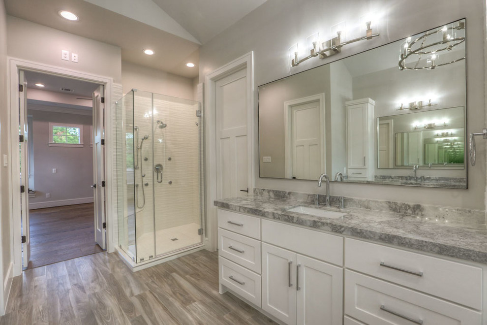 Inspiration for a large craftsman master white tile and porcelain tile medium tone wood floor and gray floor bathroom remodel in Houston with shaker cabinets, white cabinets, gray walls, an undermount sink, granite countertops and a hinged shower door