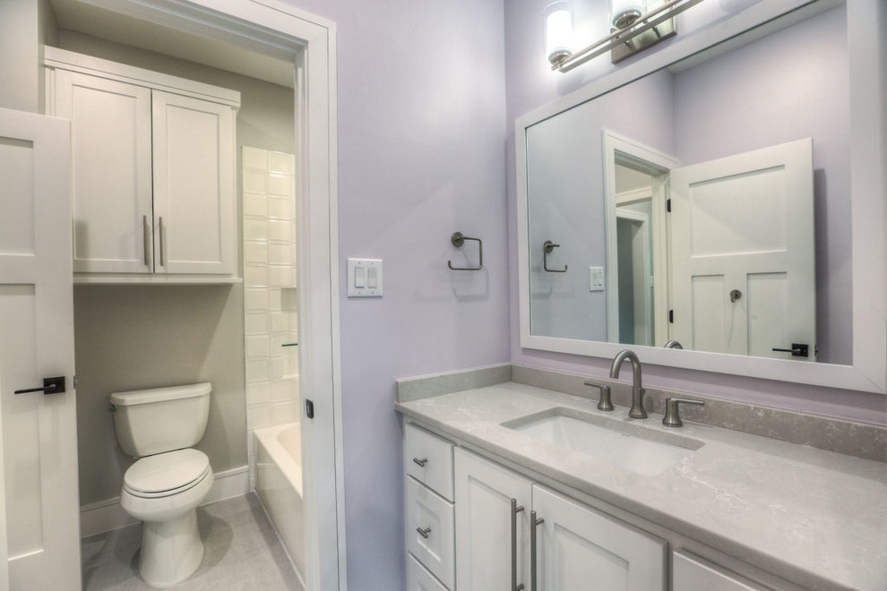 Cette image montre une salle d'eau craftsman de taille moyenne avec un placard à porte shaker, des portes de placard blanches, une baignoire en alcôve, un combiné douche/baignoire, WC séparés, un carrelage blanc, des carreaux de porcelaine, un mur violet, un sol en carrelage de céramique, un lavabo encastré, un plan de toilette en quartz modifié, un sol gris et une cabine de douche avec un rideau.