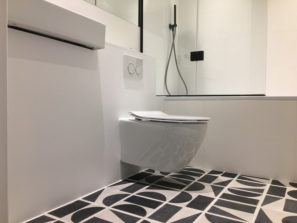 Modern inredning av ett litet badrum, med släta luckor, ett platsbyggt badkar, en dusch/badkar-kombination, en vägghängd toalettstol, svart och vit kakel, keramikplattor, vita väggar, klinkergolv i keramik, ett väggmonterat handfat och bänkskiva i akrylsten