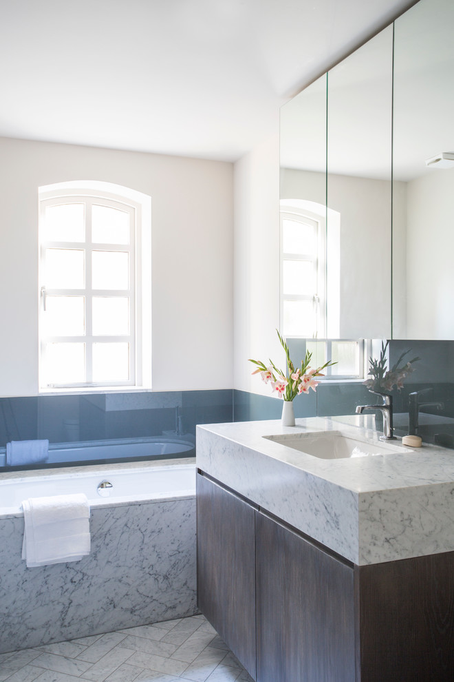 Foto de cuarto de baño actual con lavabo bajoencimera, armarios con paneles lisos, puertas de armario de madera en tonos medios, bañera encastrada sin remate y paredes blancas