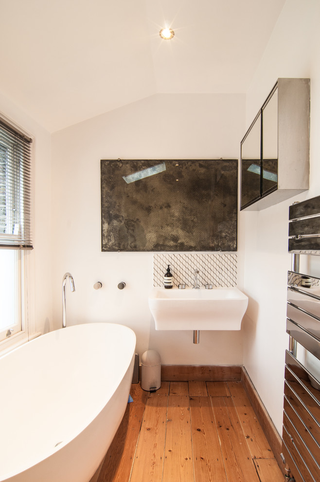 Immagine di una piccola stanza da bagno padronale nordica con vasca freestanding, WC monopezzo, pavimento in legno massello medio e lavabo sospeso