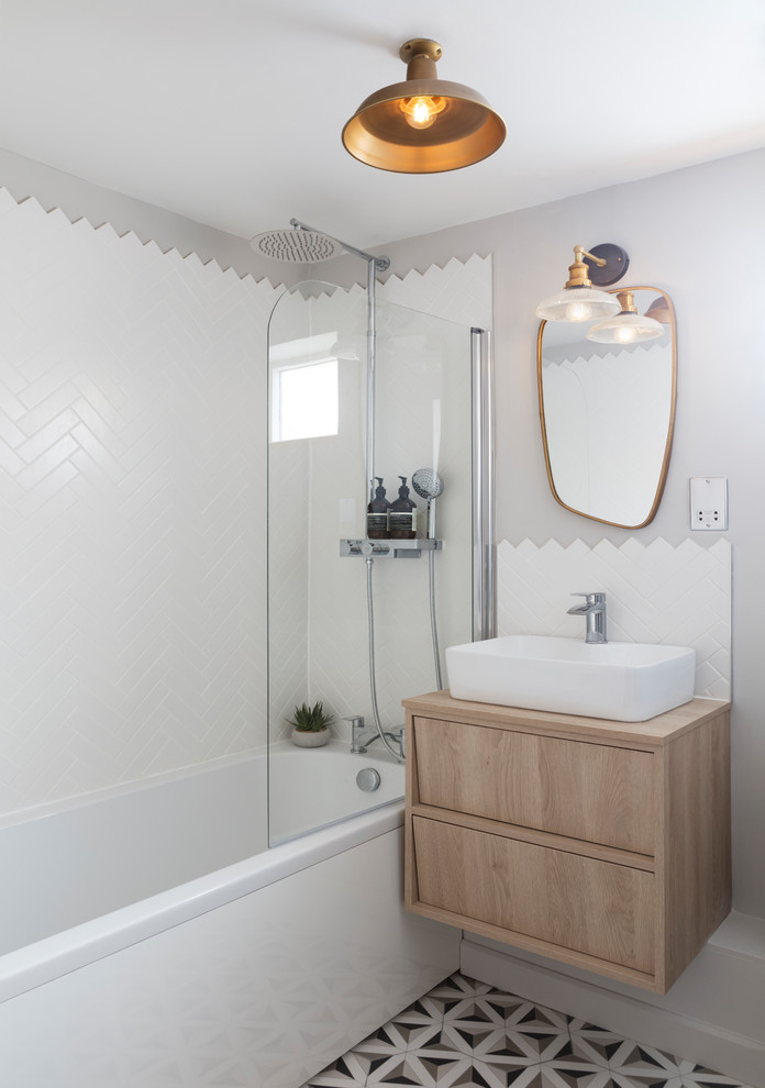 This is an example of a small contemporary family bathroom in London with light wood cabinets, an alcove bath, an alcove shower, white tiles, cement tiles, grey walls, a wall-mounted sink and wooden worktops.