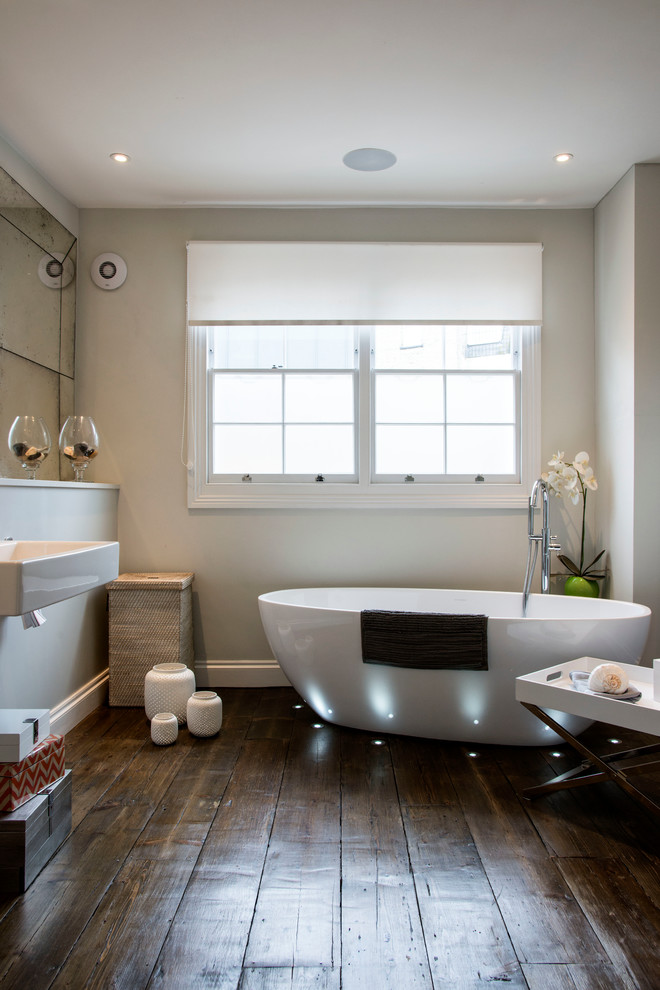 На фото: главная ванная комната среднего размера в современном стиле с подвесной раковиной, отдельно стоящей ванной, темным паркетным полом, бежевыми стенами и коричневым полом