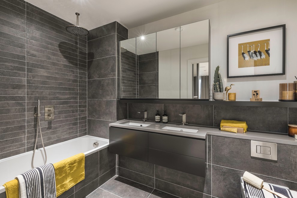 This is an example of a contemporary grey and yellow shower room bathroom in London with flat-panel cabinets, grey cabinets, a built-in bath, a shower/bath combination, a wall mounted toilet, grey tiles, grey walls, cement flooring, a submerged sink, concrete worktops, grey floors, an open shower and grey worktops.