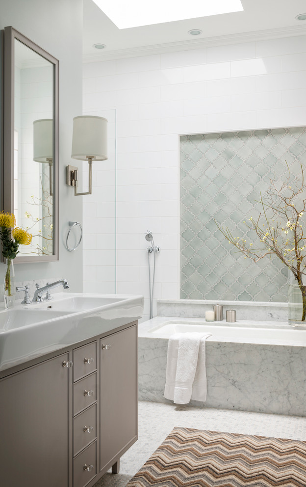 Cette image montre une salle de bain traditionnelle avec un lavabo intégré, des portes de placard grises, une baignoire encastrée, un carrelage bleu et un mur blanc.