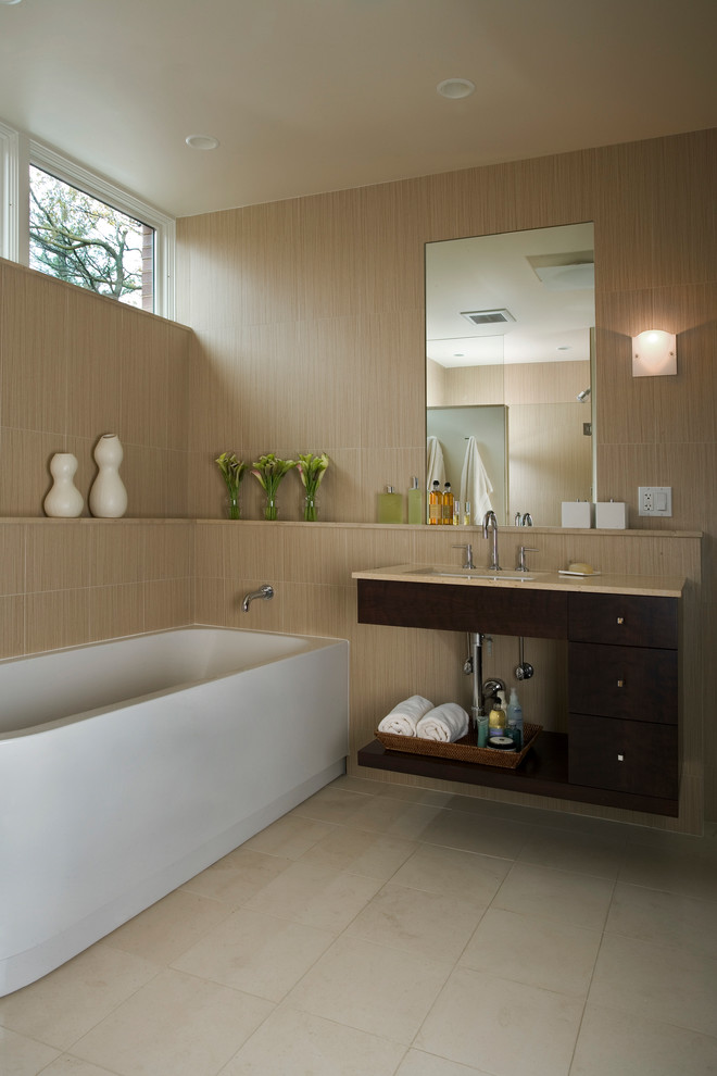 Diseño de cuarto de baño moderno con lavabo bajoencimera, armarios con paneles lisos, puertas de armario de madera en tonos medios, bañera exenta y baldosas y/o azulejos beige