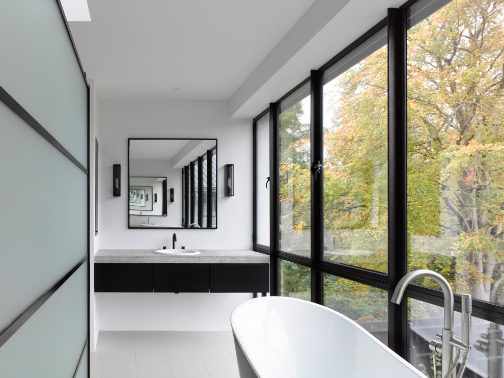 Design ideas for a large contemporary ensuite bathroom in Sussex with flat-panel cabinets, black cabinets, a freestanding bath, a walk-in shower, a wall mounted toilet, grey tiles, ceramic tiles, white walls, ceramic flooring, a built-in sink, concrete worktops, beige floors, a hinged door and grey worktops.