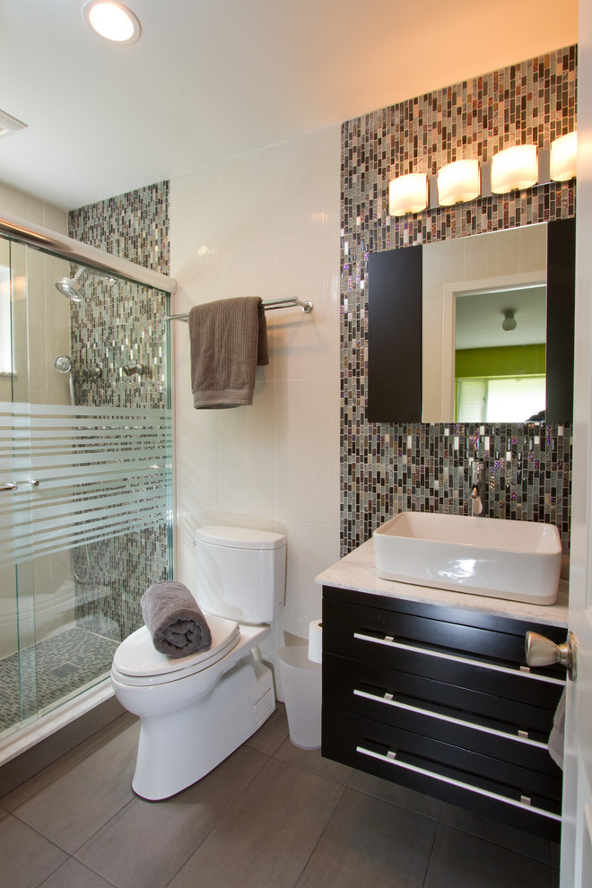 Inredning av ett modernt mellanstort badrum med dusch, med släta luckor, svarta skåp, en dusch i en alkov, en toalettstol med separat cisternkåpa, svart kakel, brun kakel, grön kakel, flerfärgad kakel, glaskakel, beige väggar, klinkergolv i porslin, ett nedsänkt handfat och marmorbänkskiva