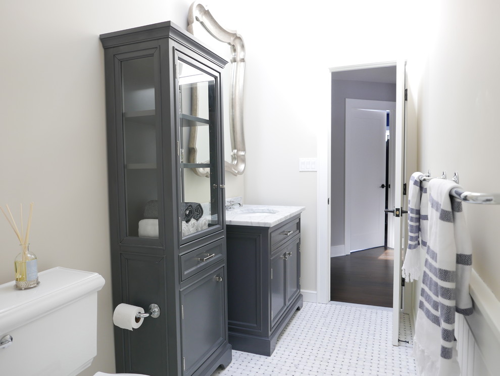 Medium sized classic family bathroom in New York with a submerged sink, flat-panel cabinets, grey cabinets, marble worktops, an alcove bath, a shower/bath combination, a two-piece toilet, white tiles, metro tiles, beige walls and marble flooring.
