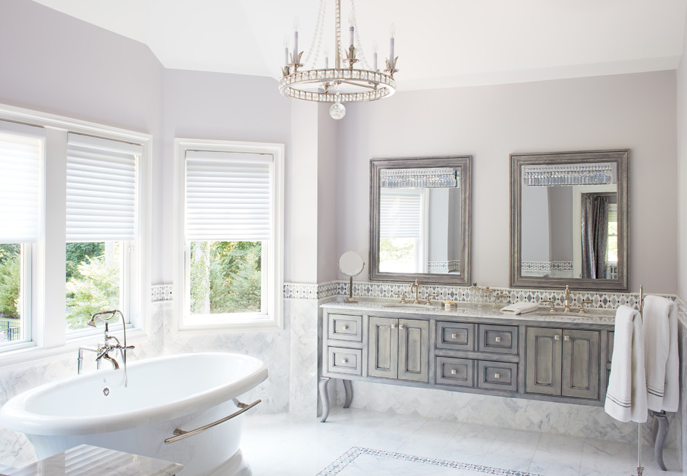 Bild på ett vintage badrum, med grå skåp, ett fristående badkar, vit kakel, grå väggar, ett undermonterad handfat och luckor med profilerade fronter
